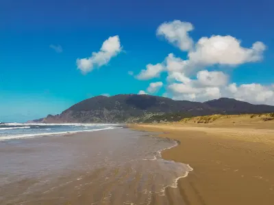 waves receding on a sandy beach with Neahkahnie Mountain and puffy clouds in the distance